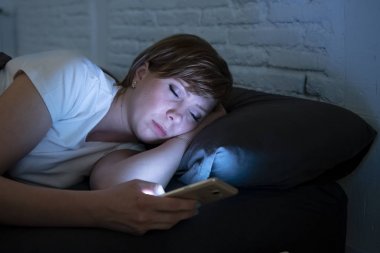 Genç çekici kadın yatakta gecenin karanlık bir odada yatan akıllı telefon kullanarak uykuya dalmak. Sohbet ve internet bağımlılığı, uykusuzluk kavramı iletileri göndermek için mobil kullanma