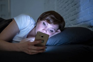 Genç çekici kadın uyanık geç gece karanlık bir yatak odasında yatakta yalan akıllı telefon kullanarak. Sohbet ve internet bağımlılığı, mobil istismar ve uykusuzluk kavramı iletileri göndermek için mobil kullanma