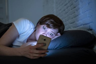 Genç çekici beyaz endişeli kadın uyanık geç gece karanlık bir yatak odasında yatakta yalan akıllı telefon kullanarak. Internet bağımlılığı mobil istismar ve uykusuzluk konsept telefon kullanarak. Seyir endişeli