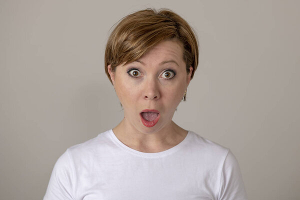 Close up portrait of a beautiful young red haired caucasian woman with a surprised face. Attractive female looking amazed with wide eyes and mouth open at the camera. Facial expressions and emotions.