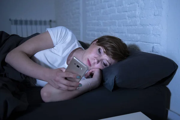 夜遅く退屈暗い寝室のベッドで横になっているスマート フォンを使用して目を覚まし若い魅力的な女性 使用してインターネット中毒 モバイル虐待と不眠症概念でメッセージを送信 チャット — ストック写真