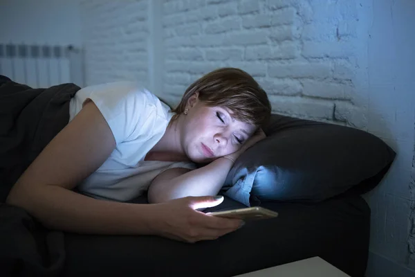 若い魅力的な白人女性は暗い寝室で夜遅くまでベッドに横たわっているスマート フォンを使用して眠りに落ちる インターネット中毒 モバイル虐待と不眠症概念で携帯電話を使用してください — ストック写真