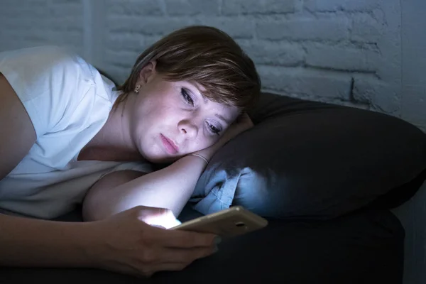 夜遅く暗い寝室のベッドで横になっているスマート フォンを使用して目を覚まし若い魅力的な女性 チャット インターネット中毒 モバイル虐待や不眠症概念でメッセージを送信する携帯電話を使用してください — ストック写真