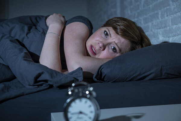 Молодая привлекательная рыжеволосая кавказская женщина, лежащая в постели поздно ночью, пытается уснуть, страдая бессонницей, кошмарами или расстройствами сна. выглядящие напряженными и изможденными
.