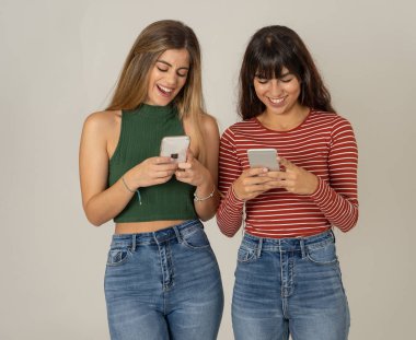 Mutlu kız arkadaşlar cep telefonundan mesajlar yolluyor sosyal medya uygulamasında sohbet ediyorlar ya da internetten alışveriş yapıyorlar. İki kadın akıllı telefonları kullanarak eğleniyor. İnsanlar, yaşam tarzı, iletişim ve teknoloji.