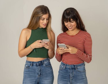 Mutlu kız arkadaşlar cep telefonundan mesajlar yolluyor sosyal medya uygulamasında sohbet ediyorlar ya da internetten alışveriş yapıyorlar. İki kadın akıllı telefonları kullanarak eğleniyor. İnsanlar, yaşam tarzı, iletişim ve teknoloji.