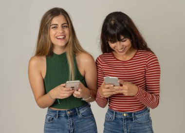 Mutlu kız arkadaşlar cep telefonundan mesajlar yolluyor sosyal medya uygulamasında sohbet ediyorlar ya da internetten alışveriş yapıyorlar. İki kadın akıllı telefonları kullanarak eğleniyor. İnsanlar, yaşam tarzı, iletişim ve teknoloji.