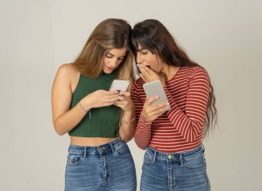 Mutlu kız arkadaşlar cep telefonundan mesajlar yolluyor sosyal medya uygulamasında sohbet ediyorlar ya da internetten alışveriş yapıyorlar. İki kadın akıllı telefonları kullanarak eğleniyor. İnsanlar, yaşam tarzı, iletişim ve teknoloji.