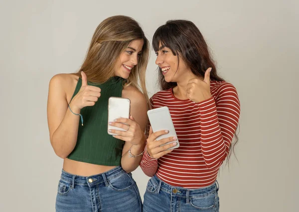 Mutlu kız arkadaşlar cep telefonundan mesajlar yolluyor sosyal medya uygulamasında sohbet ediyorlar ya da internetten alışveriş yapıyorlar. İki kadın akıllı telefonları kullanarak eğleniyor. İnsanlar, yaşam tarzı, iletişim ve teknoloji.
