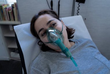 Oksijen maskeli genç çekici bir kadın üzgün ve endişeli görünüyor. Hastane yatağında akciğer kanseri teşhisi, sigara ve solunum hastalıkları ve sigara karşıtı reklam kampanyası..