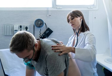 Kadın doktor hastane acil servisinde steteskopla göğsünü dinlerken oksijen maskeli genç hasta. Sigara ve solunum hastalıklarında ve tütün karşıtı reklam kampanyalarında.