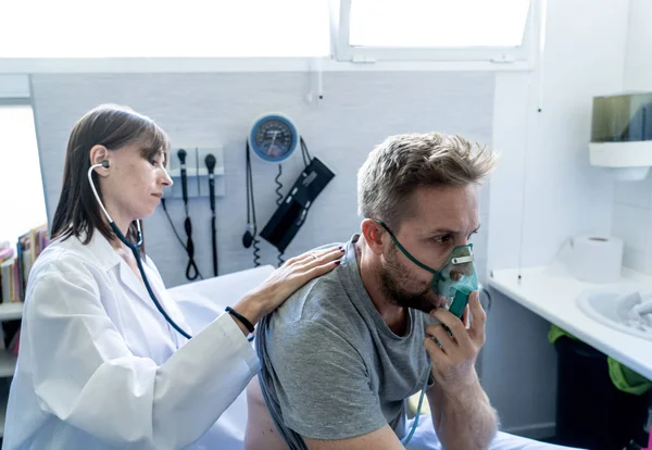 Egy Fiatal Beteg Férfi Oxigénmaszkkal Míg Női Orvos Sztetoszkóppal Hallgatja — Stock Fotó