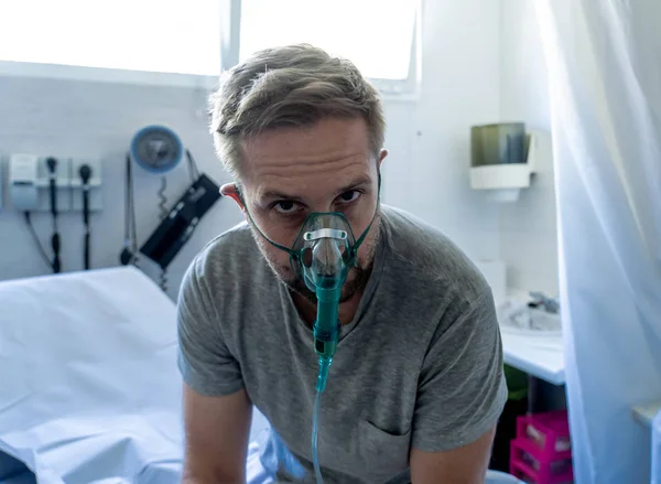 Young attractive man with oxygen mask looking sad and worried at hospital bed in clinic bedroom in lung cancer diagnose, smoking and respiratory disease and anti tobacco advertising campaign.