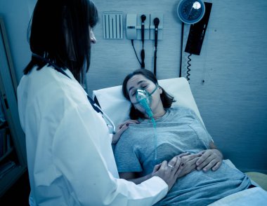 Oksijen maskesi olan genç hasta bir kadın hasta olan kadın doktor acı içinde ve hastanede endişeli görünüyor. Sağlık, sigara ve solunum hastalıklarında ve tütün reklamına karşı kampanyalarda.