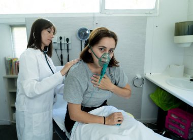 Kadın doktor hastane acil servisinde steteskopla göğsünü dinlerken oksijen maskeli genç hasta kadın. Sigara ve solunum hastalıklarında ve tütün karşıtı reklam kampanyalarında.