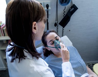 Oksijen maskesi olan genç hasta bir kadın hasta olan kadın doktor acı içinde ve hastanede endişeli görünüyor. Sağlık, sigara ve solunum hastalıklarında ve tütün reklamına karşı kampanyalarda.