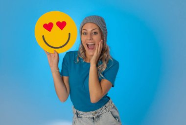 Çekici genç bir kadın Hearts Eyes ya da In Love emojisi tutuyor. Sosyal medyada paylaşırken mutlu ve heyecanlı hissediyor. Yüz ifadeleri, sosyal ağ bildirim simgesi ve teknoloji kavramı.