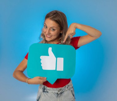 Elinde sembolik sosyal medya bildirim ikonu gibi bir şey tutan güzel genç bir kadın takipçilerden online yorumlarını, blogunu veya işini sevmelerini istiyor. İnternet saplantısı, ağ kurma ve teknoloji bağlantılarında.