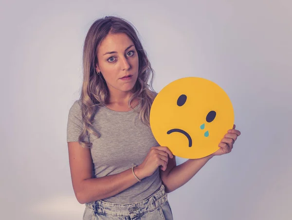Young woman holding sad crying face emoticon icon feeling unhappy about news in social media on the internet. Facial expressions, social network, notification icons and technology concept.