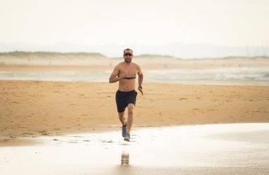 Akıllı saat ile sahilde çalışan kalp hızı monitörü ile spor fitness adam. Fit vücut erkek koşucu spor egzersiz ve teknoloji ve sağlıklı yaşam tarzı kavramı denizde koşu egzersiz yapıyor.