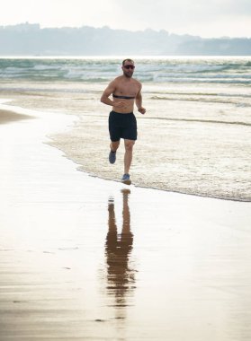 Akıllı saat ile sahilde çalışan kalp hızı monitörü ile spor fitness adam. Fit vücut erkek koşucu egzersiz egzersiz ve sağlıklı yaşam tarzı eğitim teknolojisi yenilik deniz kıyısında koşu.