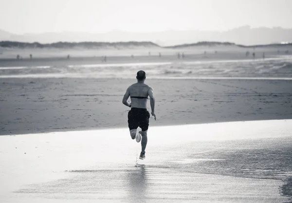 Athlete runner running with heart rate monitor and smart watch on beach. Shirtless fitness man exercising in outdoor training. Advertising style in sports technology healthcare wellness innovation.