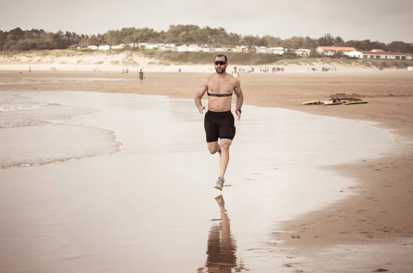 Sports fitness man with heart rate monitor running on beach with smart watch. Fit body male runner doing jogging workout at the sea in sport exercise and technology and healthy lifestyle concept.