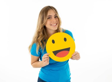 Attractive young woman holding happy face emoticon icon excited to be liked in social media in facial expressions, social network, notification icons and technology communication. clipart