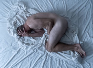 Çıplak bir adam yatakta tek başına ağlıyor üzgün ve yıkılmış hissediyor yüzünü ve cinsel organını kaplayan acı ve depresyon çekiyor. Erkeklerde cinsel yolla bulaşan hastalıklar ve testis kanseri kavramında.