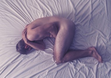 Çıplak bir adam yatakta tek başına ağlıyor üzgün ve yıkılmış hissediyor yüzünü ve cinsel organını kaplayan acı ve depresyon çekiyor. Erkeklerde cinsel yolla bulaşan hastalıklar ve testis kanseri kavramında.
