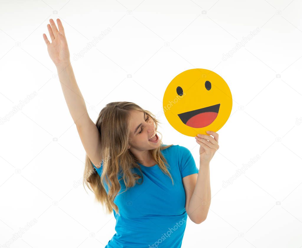 Attractive young woman holding happy face emoticon icon excited to be liked in social media in facial expressions, social network, notification icons and technology communication.