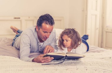 Baba ve küçük kızı birlikte kitap okuyorlar. Mutlu baba ve küçük kızın yatakta masal okurken eğlendiği bir hayat tarzı. Mutlu aile, ebeveynlik ve eğitim konseptinde.
