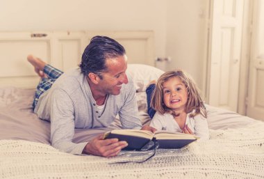 Baba ve küçük kızı birlikte kitap okuyorlar. Mutlu baba ve küçük kızın yatakta masal okurken eğlendiği bir hayat tarzı. Mutlu aile, ebeveynlik ve eğitim konseptinde.
