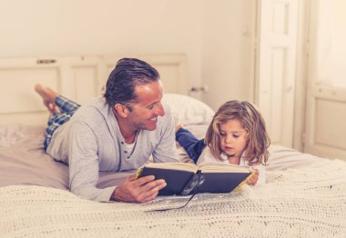 Baba ve küçük kızı birlikte kitap okuyorlar. Mutlu baba ve küçük kızın yatakta masal okurken eğlendiği bir hayat tarzı. Mutlu aile, ebeveynlik ve eğitim konseptinde.