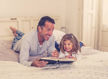 Baba ve küçük kızı birlikte kitap okuyorlar. Mutlu baba ve küçük kızın yatakta masal okurken eğlendiği bir hayat tarzı. Mutlu aile, ebeveynlik ve eğitim konseptinde.