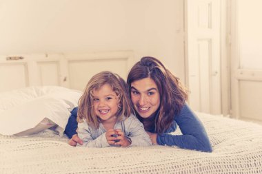 Yatakta dinlenen güzel anne ve kızın hayat tarzı portresi. Anne ve küçük tatlı kız eğleniyor, öpüşüyor ve evde sarılıyorlar. Mutlu aile, eğitim ve tek ebeveyn kavramı.