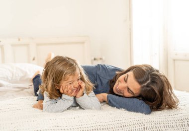 Yatakta dinlenen güzel anne ve kızın hayat tarzı portresi. Anne ve küçük tatlı kız eğleniyor, öpüşüyor ve evde sarılıyorlar. Mutlu aile, eğitim ve tek ebeveyn kavramı.