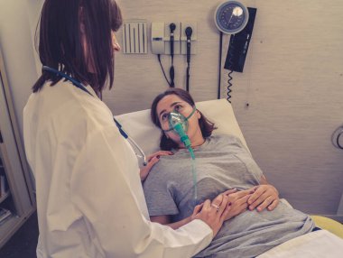 Oksijen maskesi olan genç hasta bir kadın hasta olan kadın doktor acı içinde ve hastanede endişeli görünüyor. Sağlık, sigara ve solunum hastalıklarında ve tütün reklamına karşı kampanyalarda.