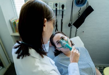 Oksijen maskesi olan genç hasta bir kadın hasta olan kadın doktor acı içinde ve hastanede endişeli görünüyor. Sağlık, sigara ve solunum hastalıklarında ve tütün reklamına karşı kampanyalarda.