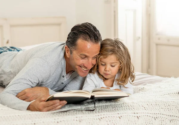 Baba ve küçük kızı birlikte kitap okuyorlar. Mutlu baba ve küçük kızın yatakta masal okurken eğlendiği bir hayat tarzı. Mutlu aile, ebeveynlik ve eğitim konseptinde.