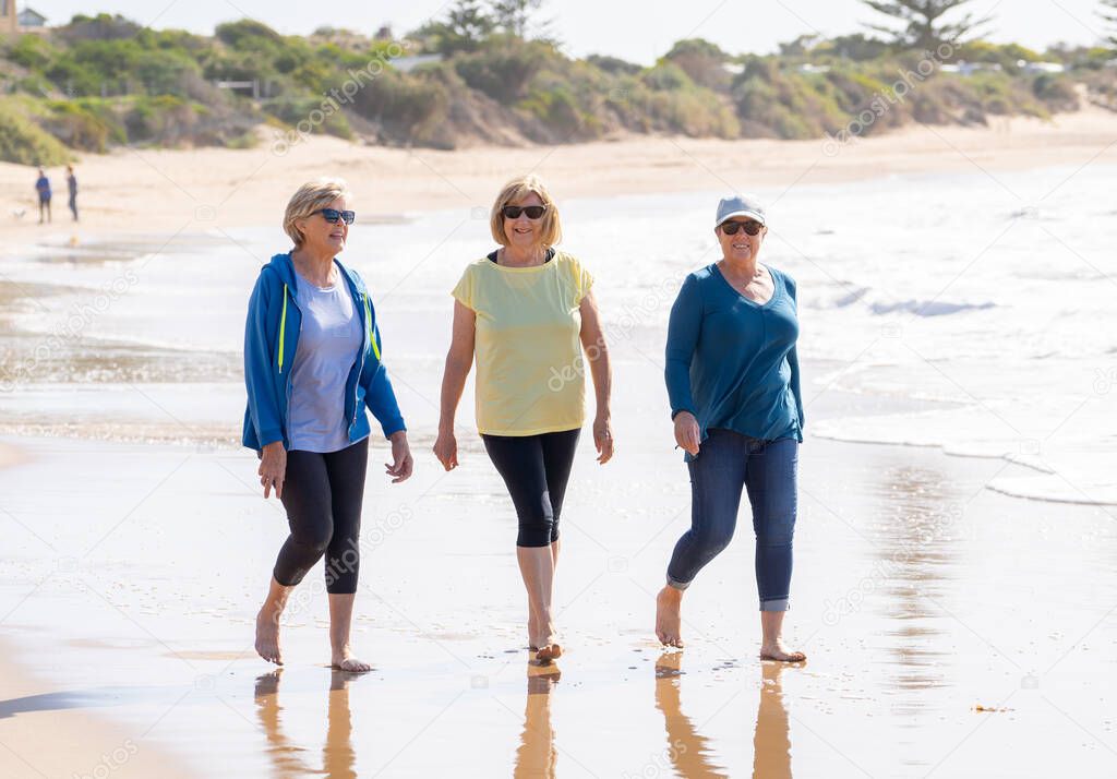 Lovely group of three senior retired woman on their 60s walking and having fun on holiday beach. Mature females Laughing enjoying friendship. In vacations and retirement lifestyle concept.