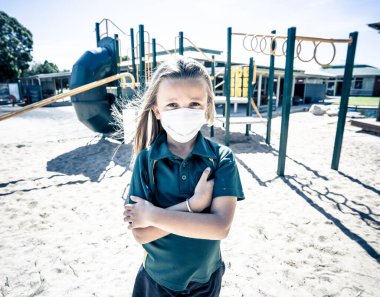 Covid-19 salgın okulları kapanıyor. Okul kapalıyken okul bahçesinde depresif ve yalnız hissetmekten sıkılmış maskeli kız öğrenci. Coronavirus önleme tedbirleri olarak kısıtlamalar ve tecrit.