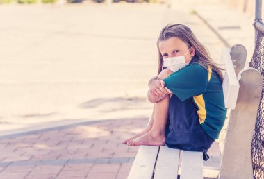 Covid-19 salgın okulları kapanıyor. Üzgün ve sıkılmış maskeli liseli kız kapalı okulunun dışında kendini depresif ve yalnız hissediyordu. Coronavirus önleme tedbirleri olarak kısıtlamalar ve tecrit.