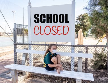 Covid-19 outbreak schools closures. Sad and bored Schoolgirl kid with face mask feeling depressed and lonely outside her closed school. Restrictions and lockdown as Coronavirus containment measures. clipart