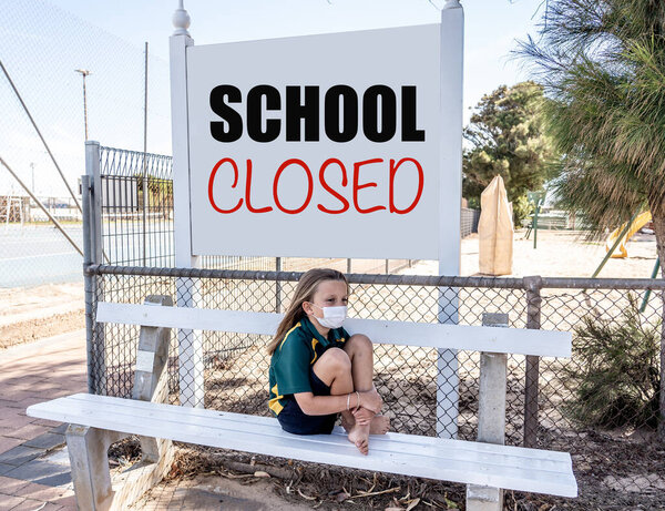 Covid-19 outbreak schools closures. Sad and bored Schoolgirl kid with face mask feeling depressed and lonely outside her closed school. Restrictions and lockdown as Coronavirus containment measures.