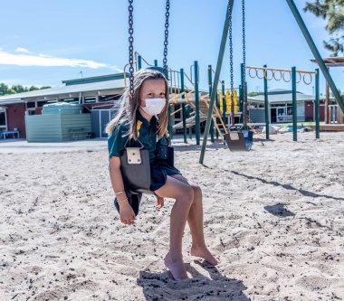 Covid-19 salgın okulları kapanıyor. Okul kapalıyken okul bahçesinde depresif ve yalnız hissetmekten sıkılmış maskeli kız öğrenci. Coronavirus önleme tedbirleri olarak kısıtlamalar ve tecrit.