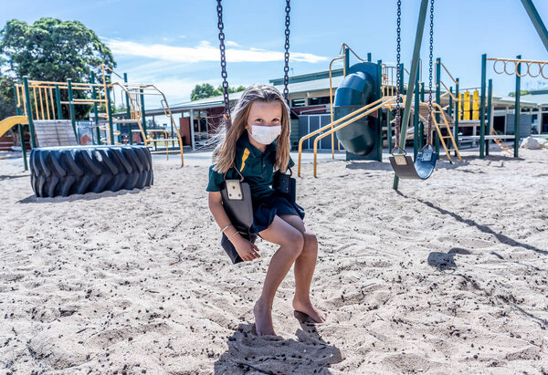Covid-19 outbreak schools closures. Sad Schoolgirl with face mask bored feeling depressed and lonely in empty playground as school is closed. Restrictions and lockdown as Coronavirus containment measures.