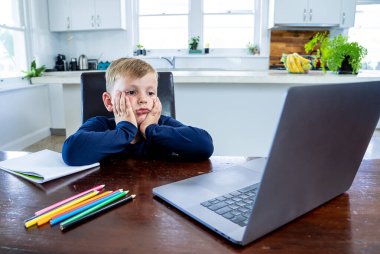 Coronavirus salgını. Kilitlenme ve okul kapanması. Yüz maskeli okul çocuğu evde sıkılmış ve depresif hissederek online eğitim dersleri izliyor. COVID-19 salgını çocukları çevrimiçi öğrenmeye zorluyor.