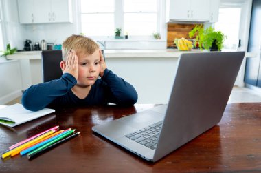 Coronavirus salgını. Kilitlenme ve okul kapanması. Yüz maskeli okul çocuğu evde sıkılmış ve depresif hissederek online eğitim dersleri izliyor. COVID-19 salgını çocukları çevrimiçi öğrenmeye zorluyor.