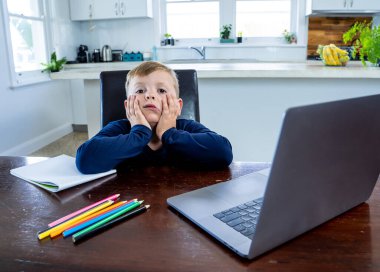 Coronavirus salgını. Kilitlenme ve okul kapanması. Yüz maskeli okul çocuğu evde sıkılmış ve depresif hissederek online eğitim dersleri izliyor. COVID-19 salgını çocukları çevrimiçi öğrenmeye zorluyor.